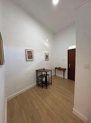 A hallway with wooden flooring, white walls, and two framed pictures. There is a small table and a door in the background. - Cozy apartment very well communicated (Madrid)