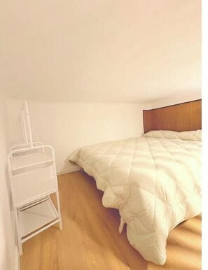 A small, single-bed room with a wooden floor and a white metal shelf unit against the wall. - Cozy apartment very well communicated (Madrid)