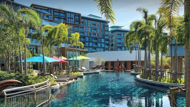 Ein Hotel mit Schwimmbad, umgeben von Palmen und modernen Gebäuden.
