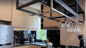 Eine moderne Küche mit Holzschränken, einer schwarzen Arbeitsplatte, einem Samsung-Kühlschrank, einer Kaffeemaschine und einem hängenden Weinkühler.