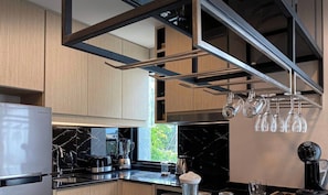 Eine moderne Küche mit Holzschränken, einer schwarzen Arbeitsplatte, einem Samsung-Kühlschrank, einer Kaffeemaschine und einem hängenden Weinkühler.