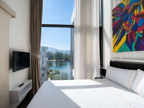 Ein Hotelzimmer mit einem großen Bett, einem Fernseher, einem Gemälde und Seeblick.