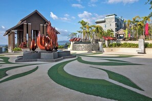 Ein Resort mit einem modernen Gebäude, einer dekorativen Metallskulptur und einer begrünten, bepflanzten Anlage mit Grünflächen und Betonmustern.