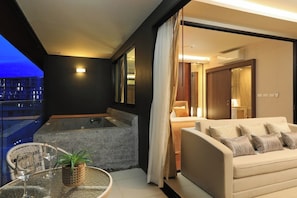 A modern interior with a sofa, a glass table with a plant, and a view of a cityscape at dusk. - 3BR Apartment Sea View Jacuzzi Surin Capital Pro (Surin)
