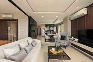 A modern living room with a sofa, armchair, coffee table, and a TV. - 3BR Apartment Sea View Jacuzzi Surin Capital Pro (Surin)