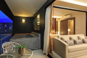 A modern hotel room with a balcony, a sofa, a small table with glasses and a plant, and a view of the cityscape at dusk. - 3BR Apartment Sea View Jacuzzi Surin Capital Pro (Surin)