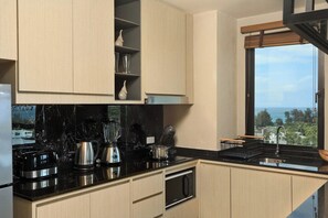 A modern kitchen with black countertops, a built-in oven, and a window with a view. - 3BR Apartment Sea View Jacuzzi Surin Capital Pro (Surin)