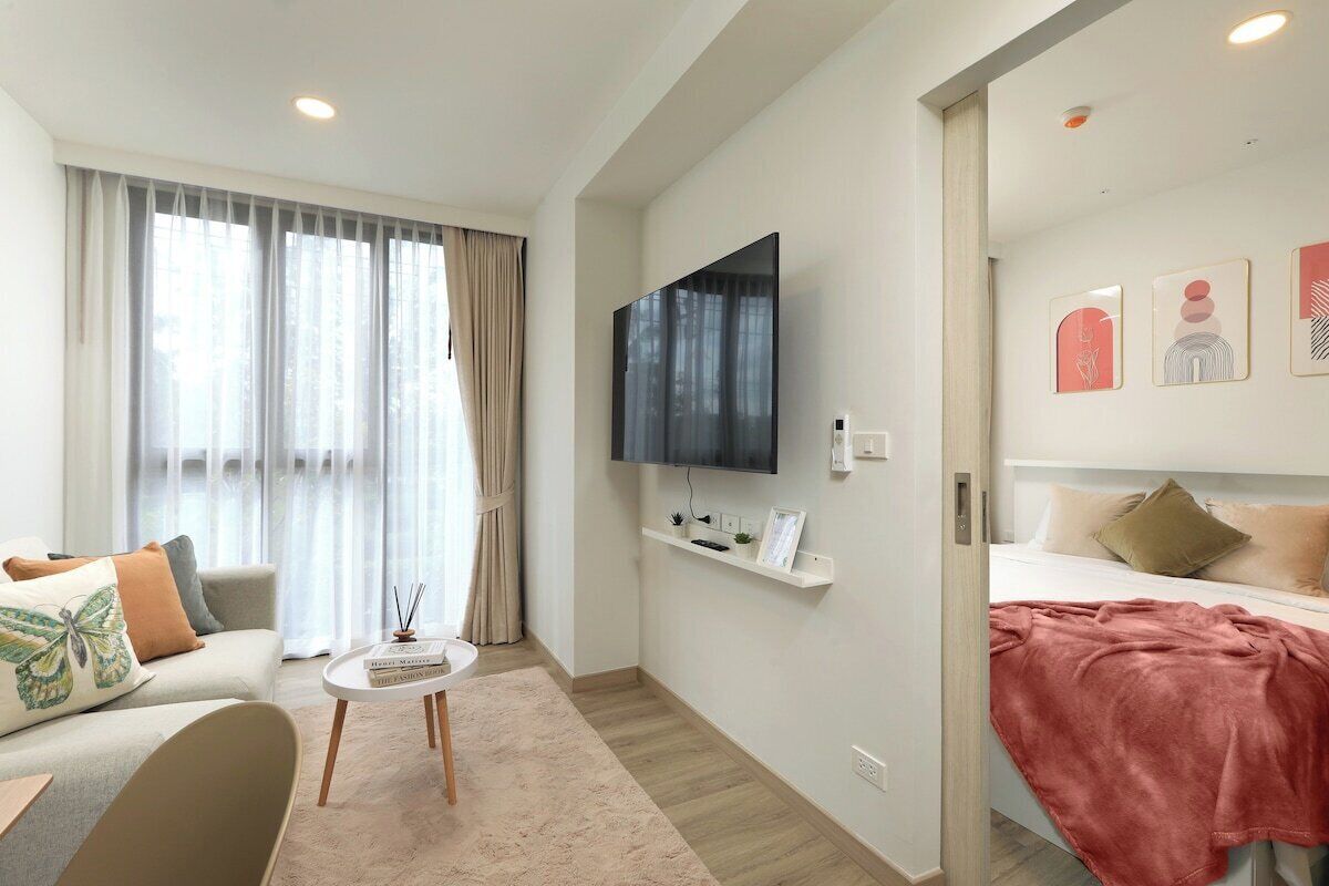 A modern hotel room with a bed, a sofa, a TV mounted on the wall, and a window with curtains.