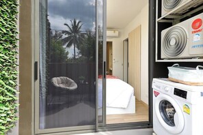 Ein modernes Zimmer mit einer Schiebeglastür, die auf einen Balkon führt, einer Waschmaschine und einer Klimaanlage.