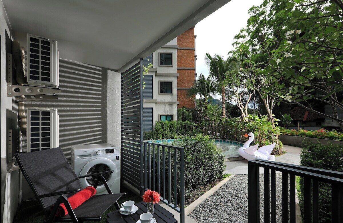 A balcony with a washing machine, a chair, a table with cups and a vase, and a swan sculpture.