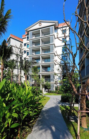 A multi-story hotel with balconies, surrounded by greenery and a paved walkway. - 1BR Apartment Pool View Naiyang Beach Capital Pro (Naiyang)