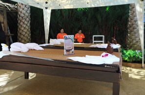 Une table de massage, agrémentée de serviettes et d’une brochure, installée à l’extérieur, avec des palmiers en arrière-plan.