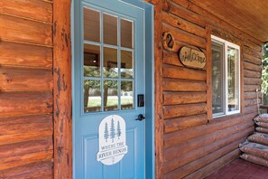 Ein Holzhaus mit blauer Tür, einem freundlichen Willkommensschild und einem Fenster mit Blick ins Freie.