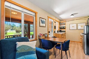 Ein gemütliches Zimmer mit einem blauen Sofa, einem Holzesstisch und Stühlen. Es gibt eine Küchenzeile mit einem Kühlschrank und einer Kaffeemaschine.