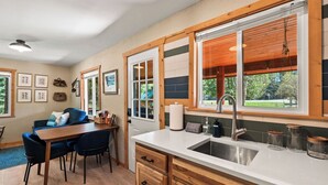 A kitchen with a wooden countertop, a sink, and a dining area with a table and chairs. - Authentic Montana log cabin, 15 min to Glacier. Queen bed + twin bunks, full kitchen & covered porch. Real adventure, real comfort — no tent required. (Martin City)