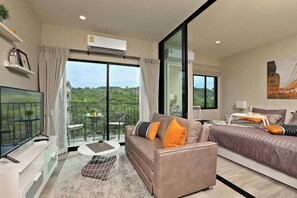 Ein modernes Hotelzimmer mit Balkon, einer Couch, einem Bett, einem Fernseher und einem Essbereich.