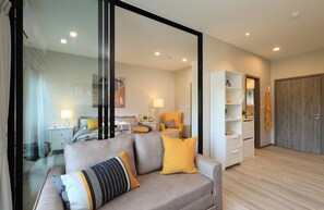 Ein modernes Wohnzimmer mit Sofa, Glastrennwand, Bett und Kleiderschrank.