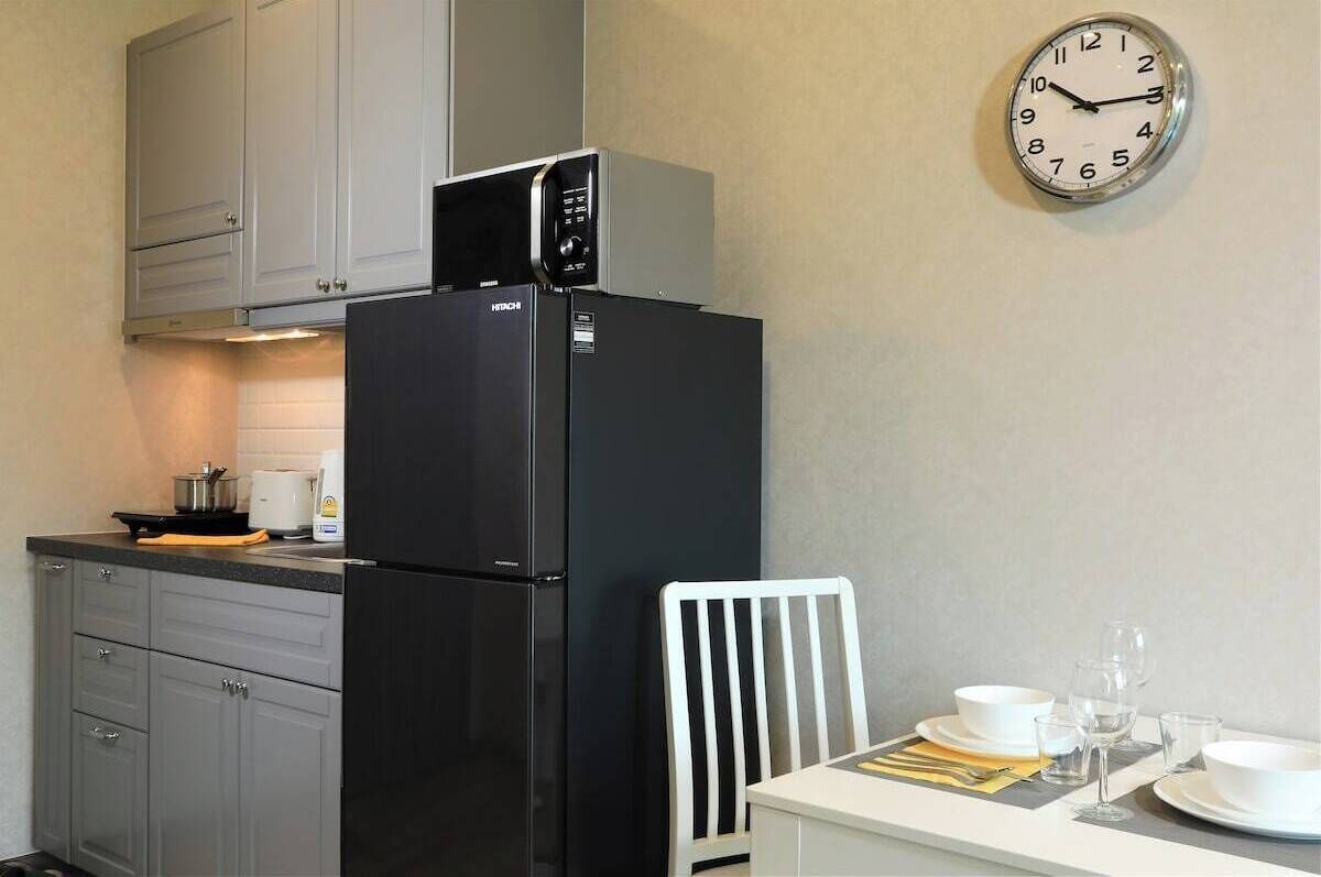 A kitchen with a black refrigerator, a microwave, a clock, and a dining table set with white dishes and glasses.