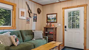 Et hyggeligt rum med en grøn sofa, en træbænk, en guitar, et indrammet billede og en dør med et vindue.