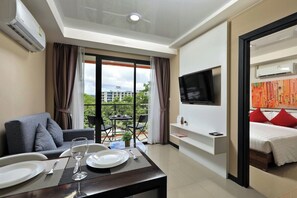 Ein Hotelzimmer mit Essbereich, einem Bett mit roten Kissen, einem Fernseher und einer Klimaanlage.