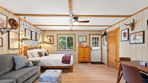Una habitación con cama, sofá, mesa de comedor de madera, aparador de madera y una puerta que da a otra habitación.