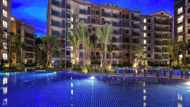 Une piscine au sol carrelé, entourée d’immeubles à plusieurs étages dotés de balcons, sous un ciel dégagé.