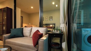 A living room with a sofa, a small table, a washing machine, and a glass partition. - Mountain View Apart Naiyang Beach B704 (Naiyang)