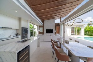Eine moderne Küche mit Marmorarbeitsplatten, einem Einbauofen und einem Essbereich mit Blick auf einen Pool.
