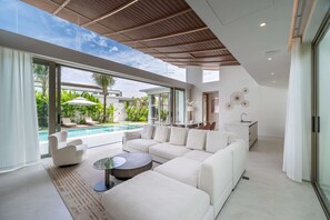 Ein modernes Wohnzimmer mit Pool, weißen Möbeln und Blick ins Freie.
