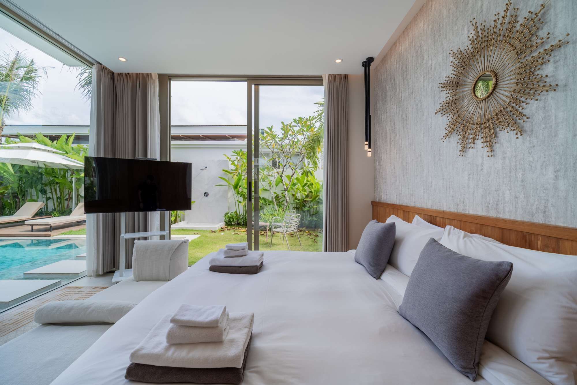 Une chambre d’hôtel moderne dotée d’un grand lit, d’une télévision à écran plat et offrant une vue sur une piscine et un jardin.