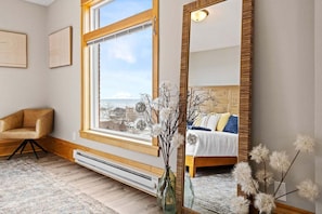 A bedroom with a large window, a bed with pillows, a chair, and a mirror.
