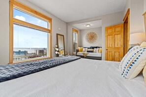 A bedroom with a large bed, a wooden door, a window with a view, and a decorative wall piece.