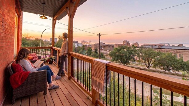 Eine Holzterrasse mit Geländer, einer Ziegelwand und Blick auf eine Stadtansicht.