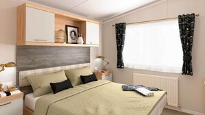 Un dormitorio con cama, mesitas de noche, cómoda, ventana con cortinas y radiador.