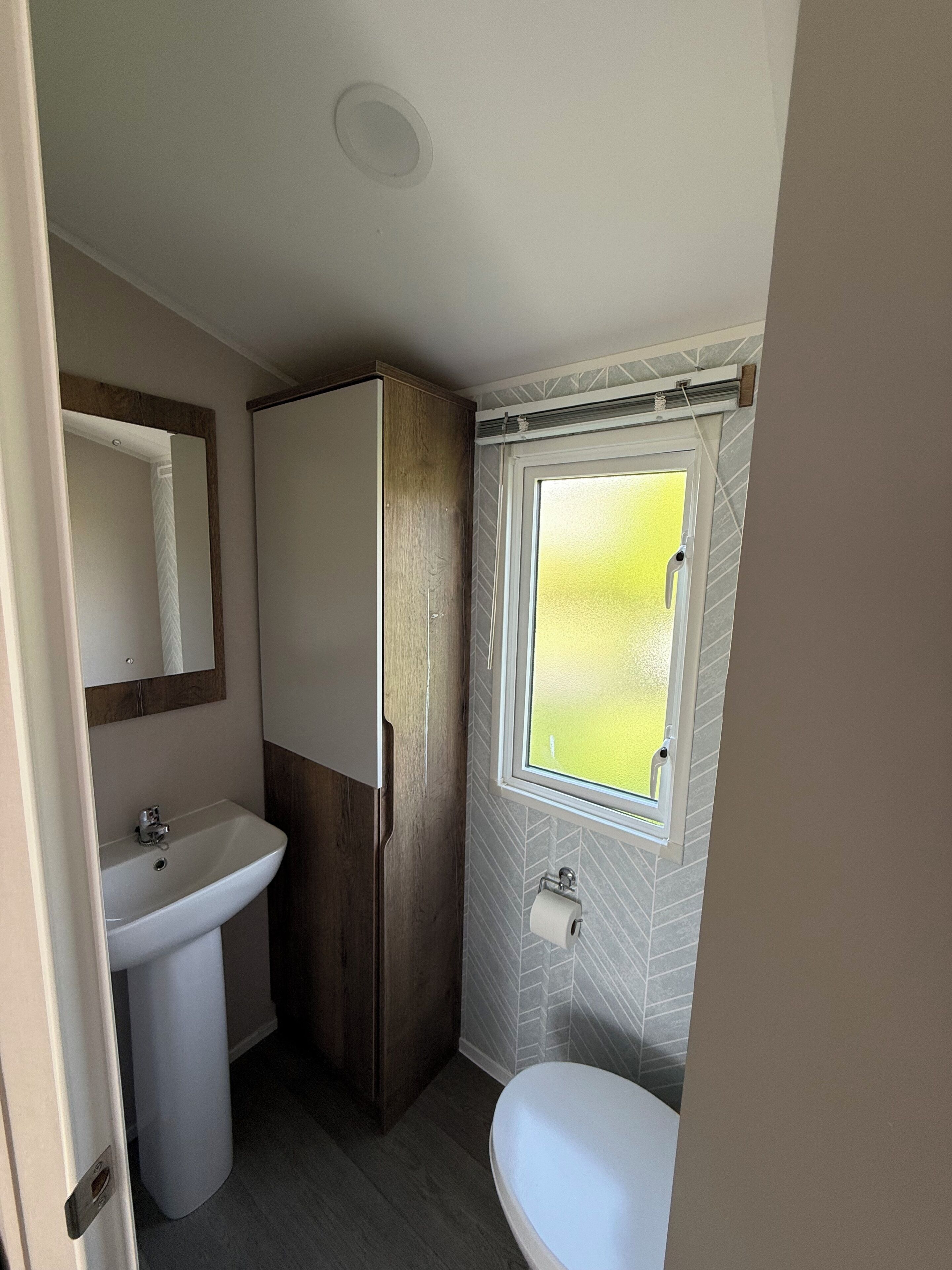 A compact bathroom with a sink, toilet, and a window with a view.