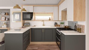 Una cocina moderna con armarios oscuros, encimera blanca, microondas, lavabo y estufa.
