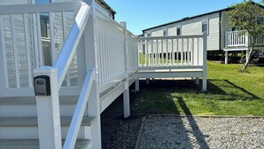 A white building with a covered outdoor area, a gravel path, and a wooden deck.
