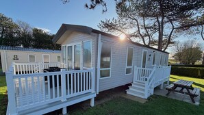 A mobile home with a porch, a deck, and a picnic table.