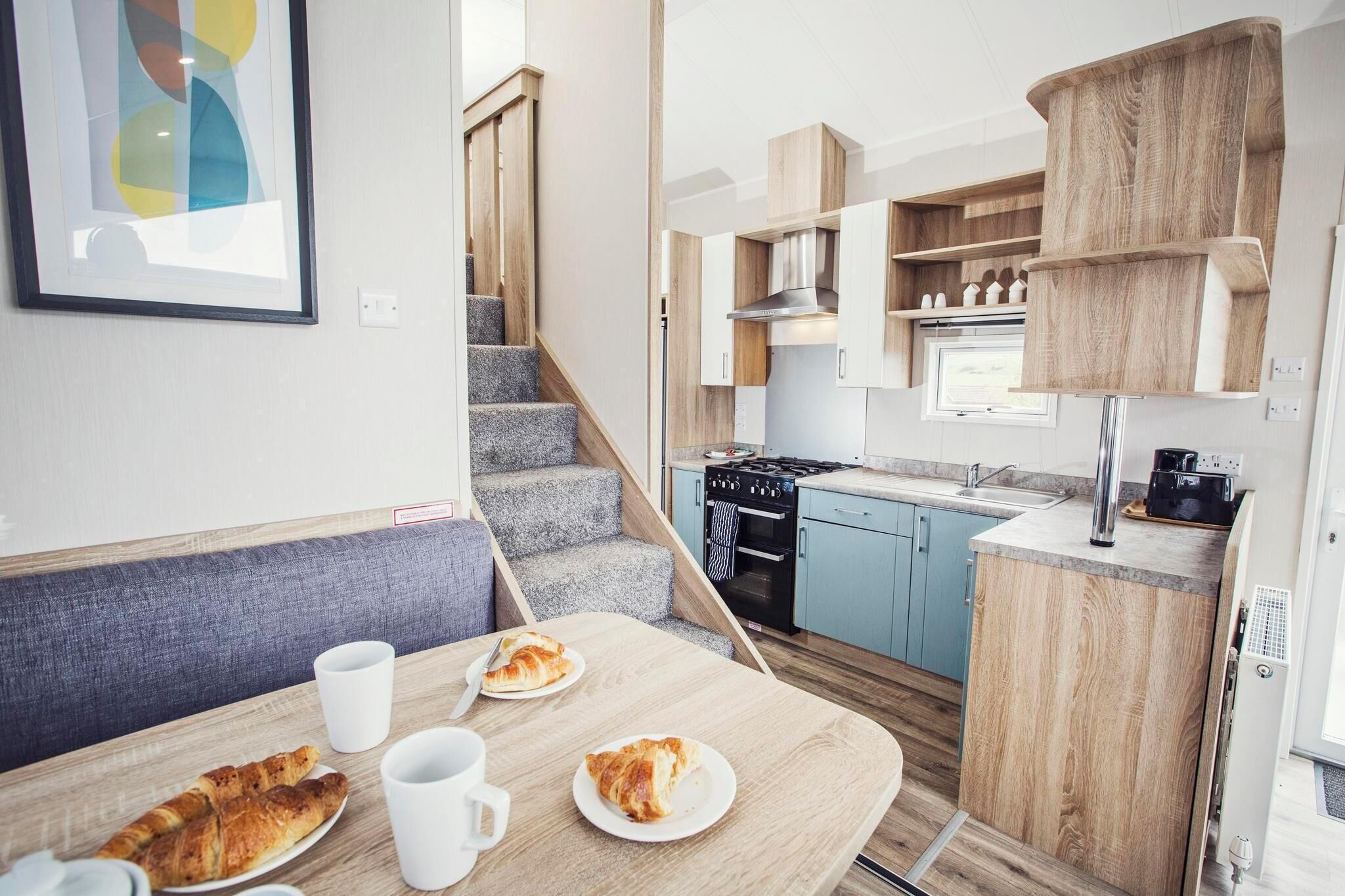 Une cuisine compacte dotée d’un four encastré, un coin repas avec un banc et un escalier menant à un autre niveau.