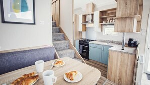 Una cocina compacta con horno integrado, un comedor con banco, y una escalera que sube a otro nivel.