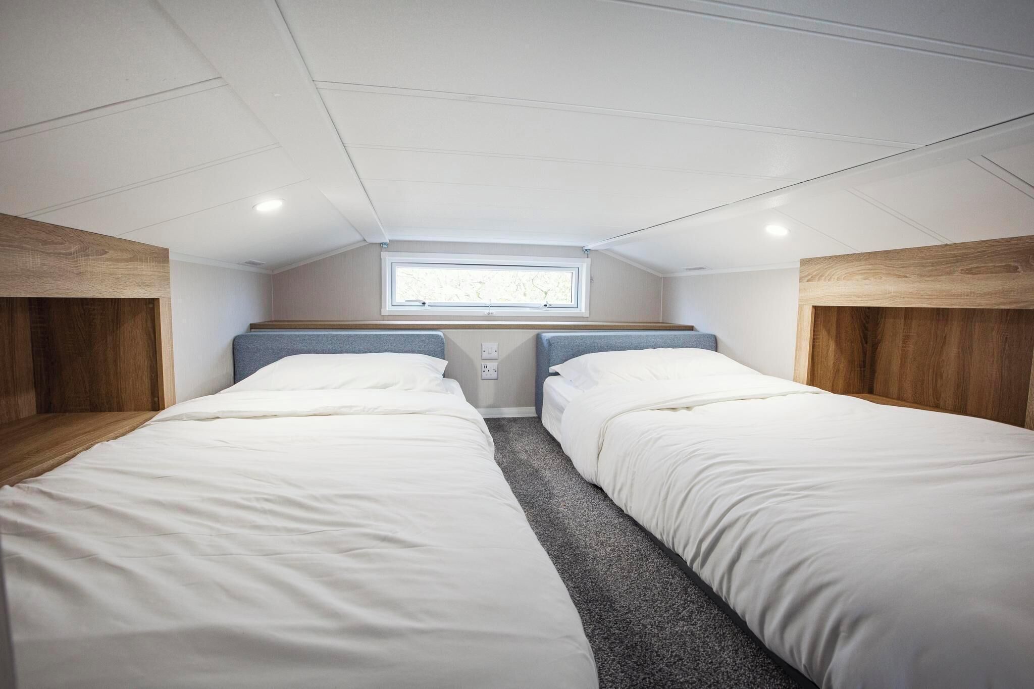 Een compacte kamer met twee bedden, een dakraam en een klein raam.
