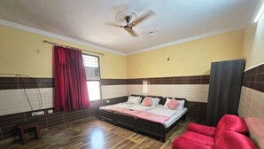 Un dormitorio con una cama, un sofá rojo, un ventilador de techo y una ventana con cortinas.
