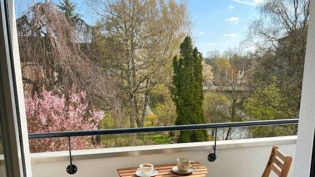 Un balcón con una mesa y dos sillas, con vistas a un paisaje escénico de árboles y una masa de agua.