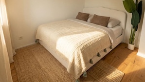 Un dormitorio con una cama, una planta grande en maceta y un aplique de pared.