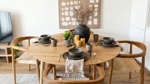 A round wooden dining table with a chandelier above, surrounded by wooden chairs with woven seats. - Riverfront Apt | Balcony | Zurich Airport | WiFi (Opfikon)