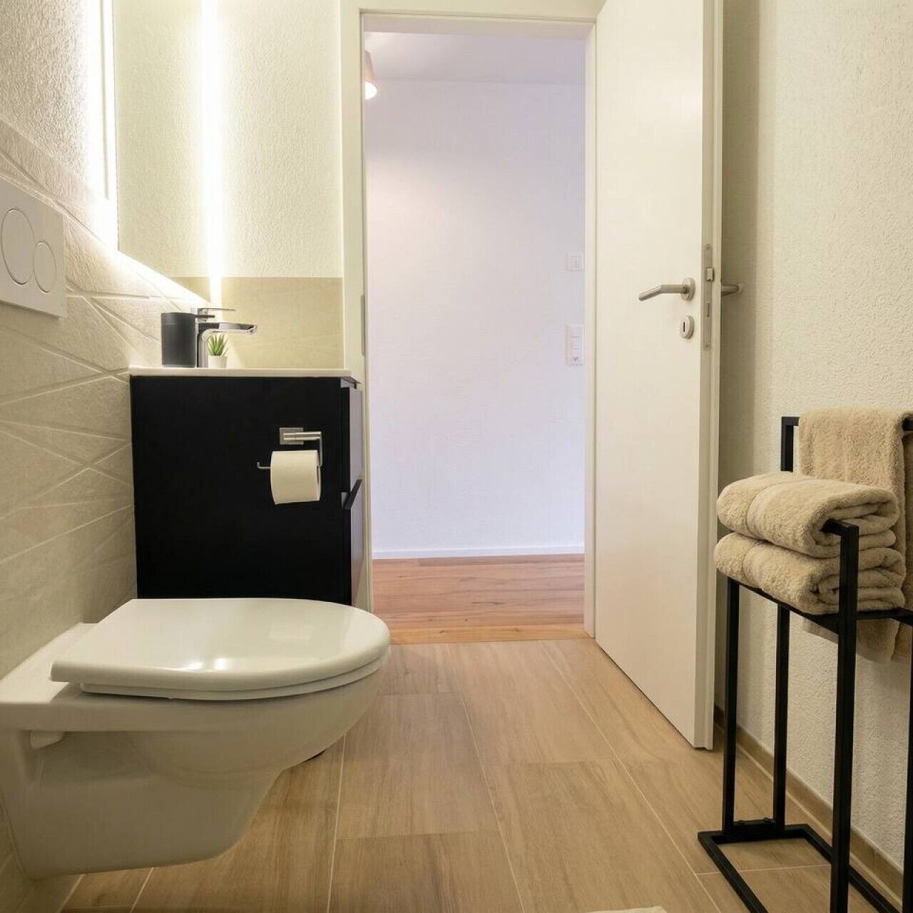 A modern bathroom with a toilet, a black cabinet, a towel rack, and a wooden floor.