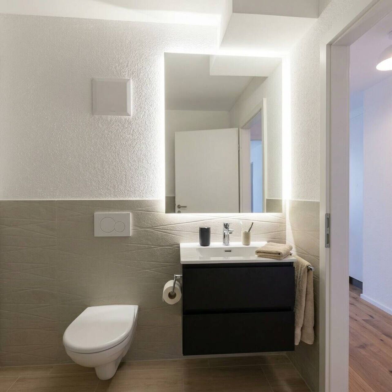 Ein modernes Badezimmer mit Toilette, Waschbecken mit Spiegel und Handtuchhalter.