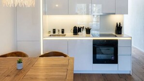 A modern kitchen with white cabinetry, a wooden dining table, a built-in oven, and a pendant light. - Riverfront Apt | Balcony | Zurich Airport | WiFi (Opfikon)