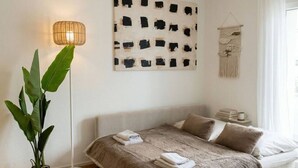 Ein Schlafzimmer mit Bett, Stehlampe, Wandkunst, einer Makramee-Aufhängung und einem Blumentopf.