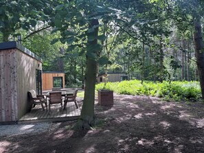 A wooden cabin with a deck, surrounded by dense forest.